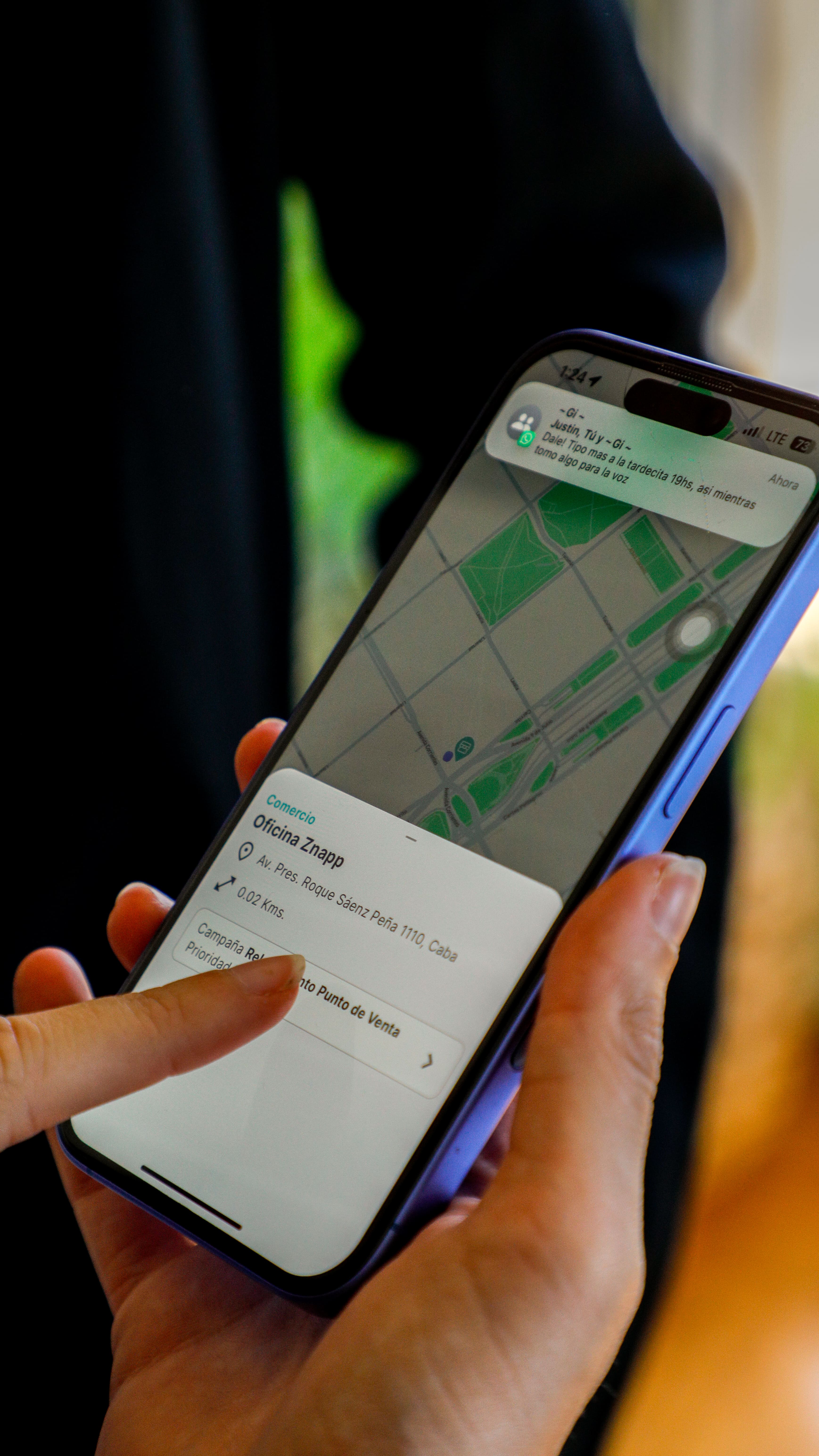 Hand holding a smartphone showing a map with the location 'Oficina Znapp' and a finger pointing at a button labeled 'Campaña Relacionado Punto de Venta'.